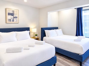 Habitación de hotel con dos camas, una mesita de noche con lámpara y una ventana con cortinas.