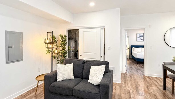 A modern living room with a dark grey sofa, a small side table, a glass coffee table, and a potted plant. - Inviting 2BD | Sleeps 6 | Northern Liberties (Philadelphia)