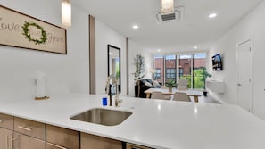 Una cocina moderna con una isla grande, un área de comedor con una mesa y sillas, un ventanal con vistas, y un televisor montado en la pared.