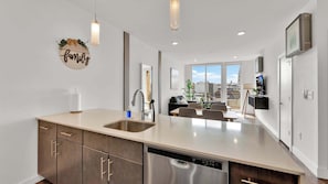 A modern kitchen with a dishwasher, a sink, and a dining area with a view.