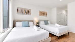 A hotel room with two beds, a nightstand with a lamp, and artwork on the walls.