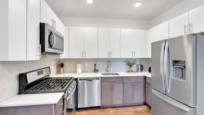 A modern kitchen with stainless steel appliances, white cabinets, and a wooden countertop.