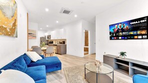 Una sala de estar moderna con un sofá, una mesa de centro y un televisor en la pared mostrando un canal deportivo.