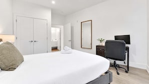 A hotel room with a bed, a desk with a chair, a TV, and a mirror on the wall.