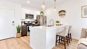 Una cocina moderna con armarios blancos, electrodomésticos de acero inoxidable y una isla central con taburetes de bar.