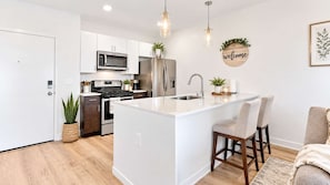 A modern kitchen with white cabinetry, stainless steel appliances, and a central island with bar stools.