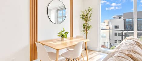 Una habitación moderna con una mesa de comedor de madera, sillas blancas, un espejo redondo y una planta en maceta.