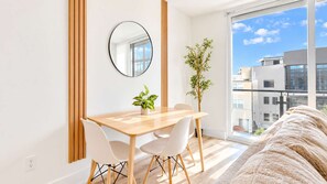 Une pièce moderne avec une table à manger en bois, des chaises blanches, un miroir rond et une plante en pot.