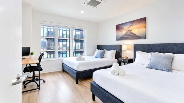 A hotel room with two beds, a desk, and a large window.
