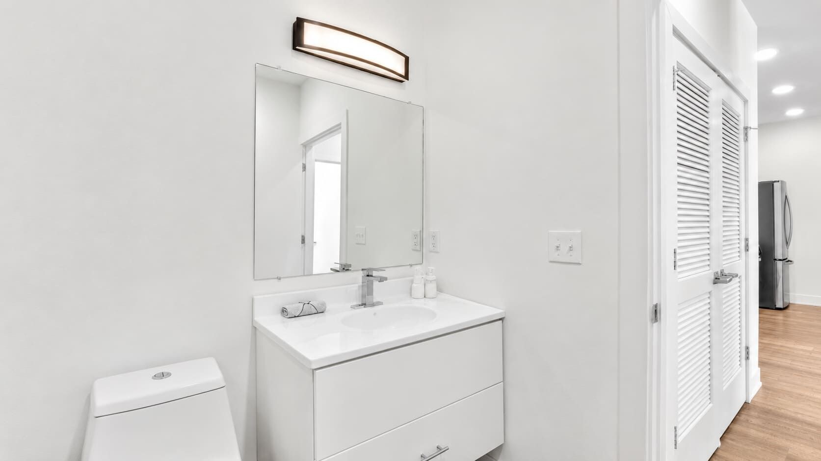 A modern bathroom with a white vanity, a large mirror, and a toilet.