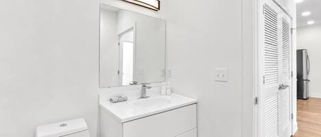 A modern bathroom with a white vanity, a large mirror, and a toilet.