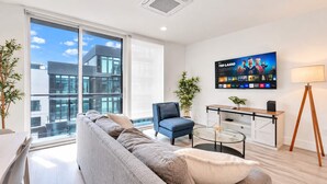 Una sala de estar moderna con un sofá, un sillón, una mesa de centro, un televisor montado en la pared y una lámpara.