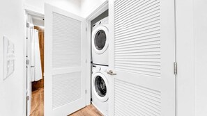 Une buanderie équipée de deux machines à laver superposées, une porte à persiennes et un plancher en bois.