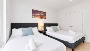 Una habitación de hotel con dos camas, una mesita de noche con lámpara, un cuadro en la pared y una puerta.