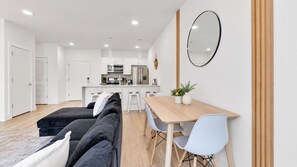 A modern living room with a sofa, dining table, and chairs. There is a kitchen area in the background with cabinets and appliances. - Luxe 1BD Near Reading Terminal | Comfort Fits 4 (Philadelphia)