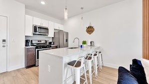 A modern kitchen with white cabinetry, stainless steel appliances, and a central island with bar stools.