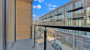A modern building with large windows and balconies, a clear sky, and a street view.