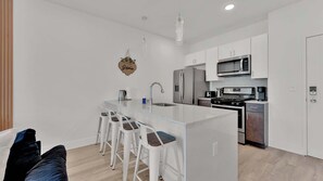Une cuisine moderne dotée d’un îlot central, d’appareils électroménagers en acier inoxydable et de meubles de rangement blancs.