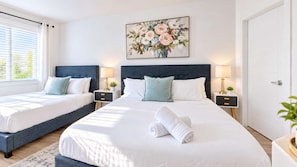 Une chambre d’hôtel avec deux lits, un grand tableau au-dessus des lits et une vue sur l’extérieur par la fenêtre.