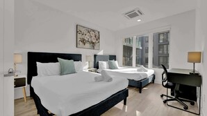 Habitación de hotel con una cama grande, dos mesitas de noche con lámparas, un escritorio con silla y una ventana con vistas a edificios.