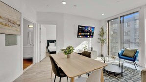 Una sala moderna con un televisor grande, una mesa de comedor y una silla azul.