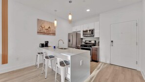A modern kitchen with a central island, bar stools, stainless steel appliances, and a painting on the wall. - Cozy 1BD | Sleeps 2 | Northern Liberties (Philadelphia)