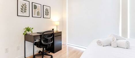 Una habitación de hotel con cama, escritorio con silla, lámpara y cuadros en la pared.