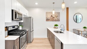 A modern kitchen with stainless steel appliances, a white countertop, and a dining area with a table and chairs.