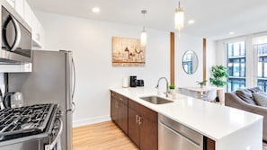 A modern kitchen with a central island, stainless steel appliances, and a dining area with a sofa and table.