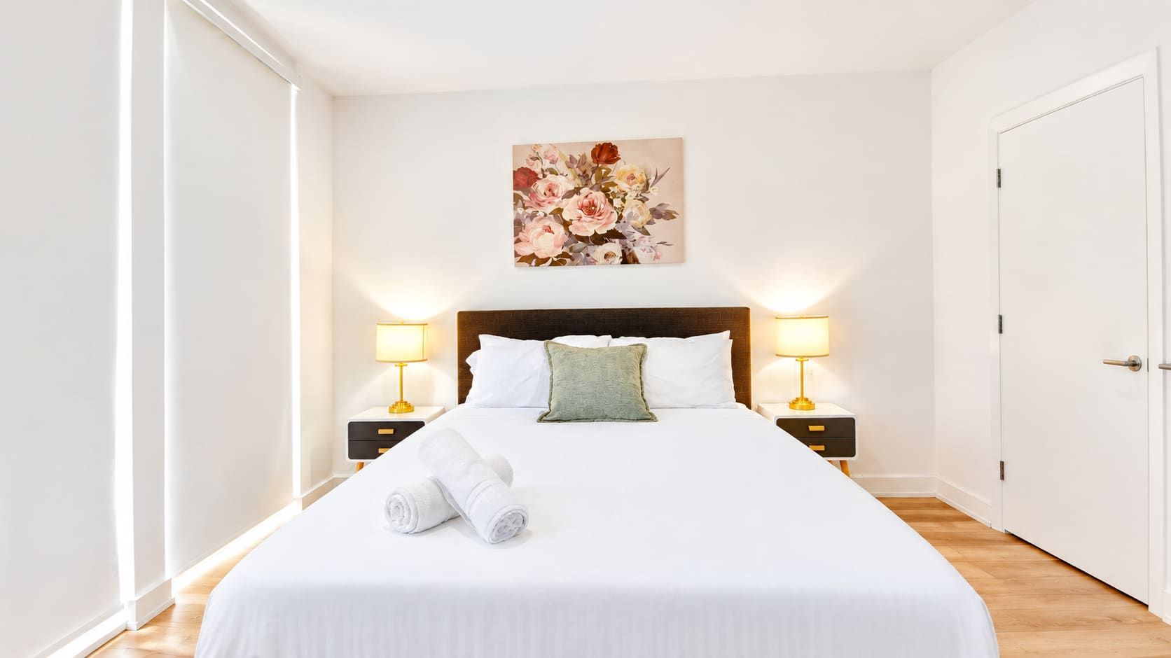 Habitación de hotel con una cama grande, dos mesitas de noche con lámparas, un cuadro en la pared y una puerta a la derecha.