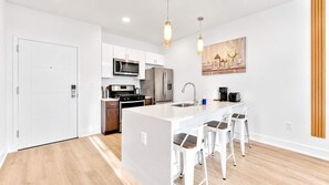 A modern kitchen with white cabinetry, stainless steel appliances, and a central island with bar stools. - Stylish 1BD Near Schuylkill River | Fits 2 Comfort (Philadelphia)