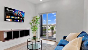 A modern living room with a flat-screen TV, a sofa, a small table, and a potted plant.