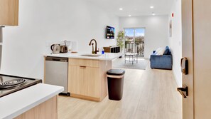 A modern kitchen with a dishwasher, a sink, and a stove. There is a dining area with a blue sofa and a view of the city through large windows.