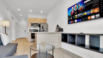 Een moderne woonkamer met een flatscreen televisie aan de muur, een glazen salontafel en een grijze bank.