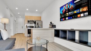 A modern living room with a flat-screen TV mounted on the wall, a glass coffee table, and a grey sofa.
