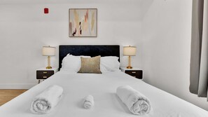 A hotel room with a large bed, two bedside tables with lamps, a painting on the wall, and a view of the outside. - Comfy 1BR Retreat by Liberty Bell | Perfect for 2 (Philadelphia)
