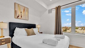 A hotel room with a large bed, two bedside tables with lamps, a painting on the wall, and a window with curtains.