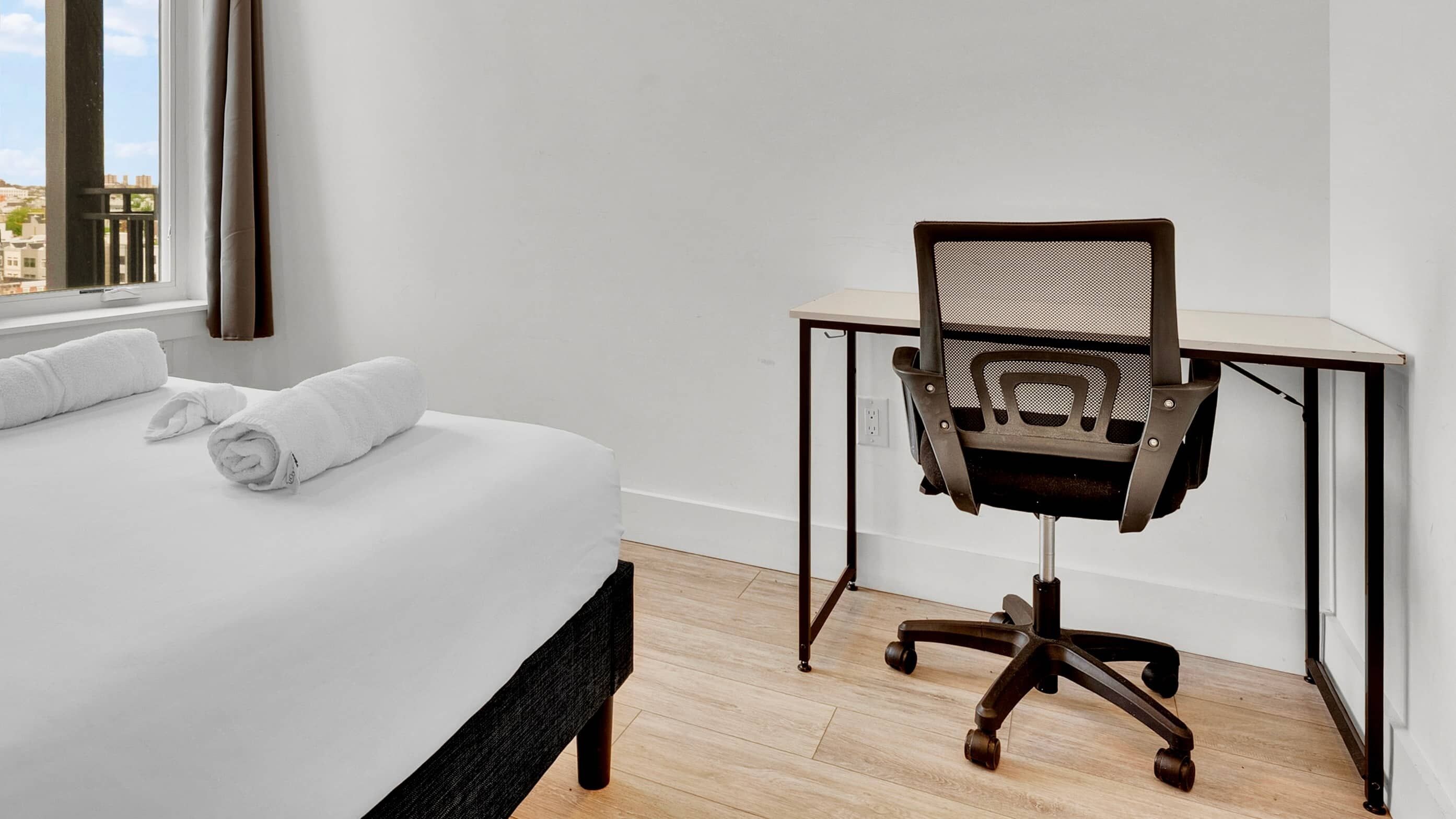 A hotel room with a bed, a desk, and a chair.