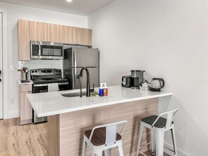 A modern kitchen with a central island, stainless steel appliances, and two white bar stools.