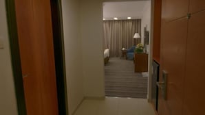 A hotel hallway leading to a room with a bed, a desk, and a lamp. - Al Massa Grand Hotel (Makkah)