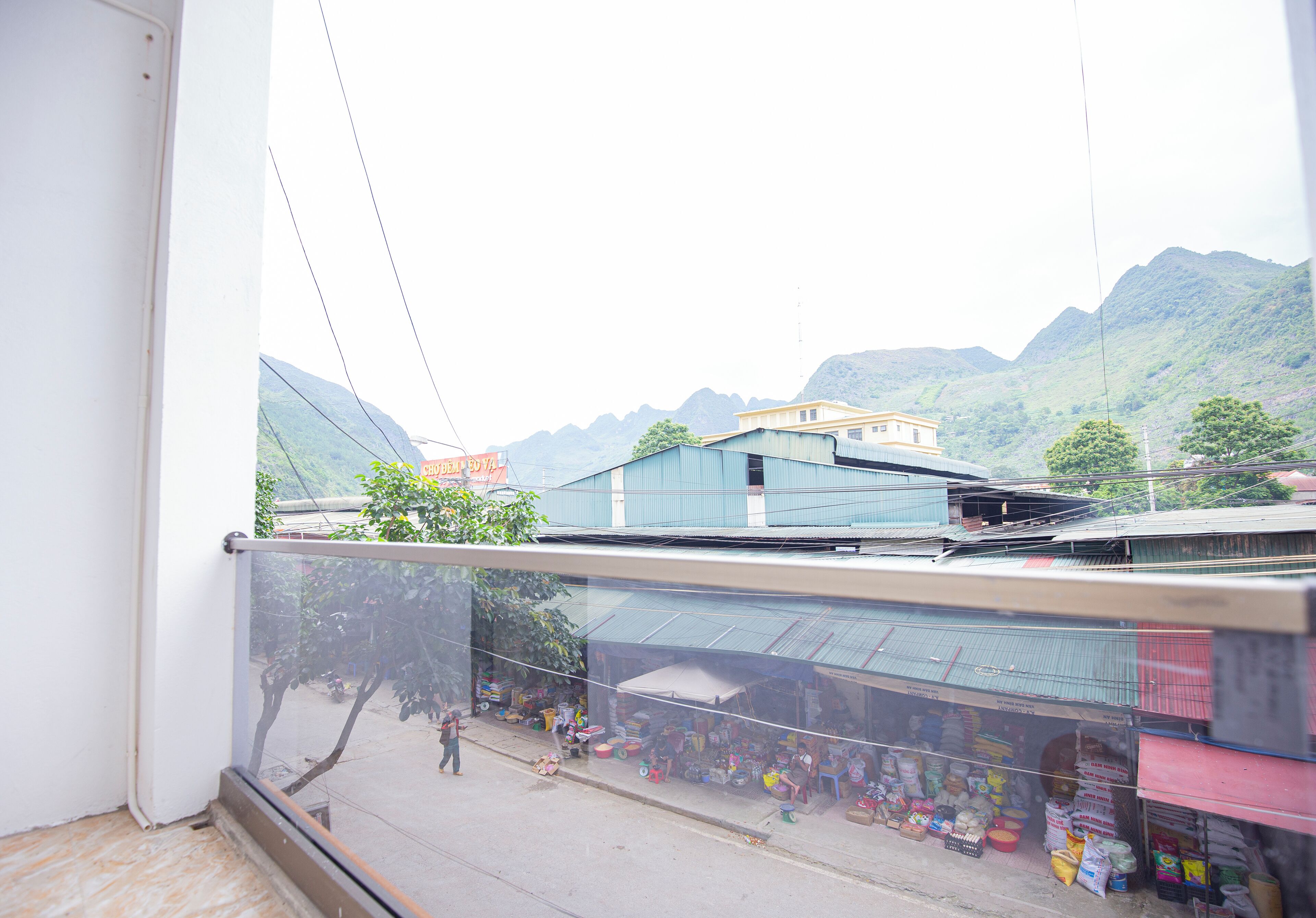 Un balcón con vista a un mercado callejero y montañas al fondo.