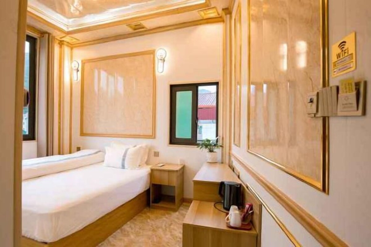 A hotel room with a large bed, bedside table, and a small desk with a chair.