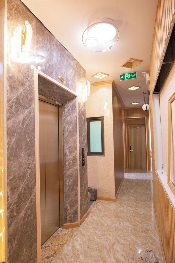 A hallway with marble flooring, a wooden-framed elevator, and a green directional sign.