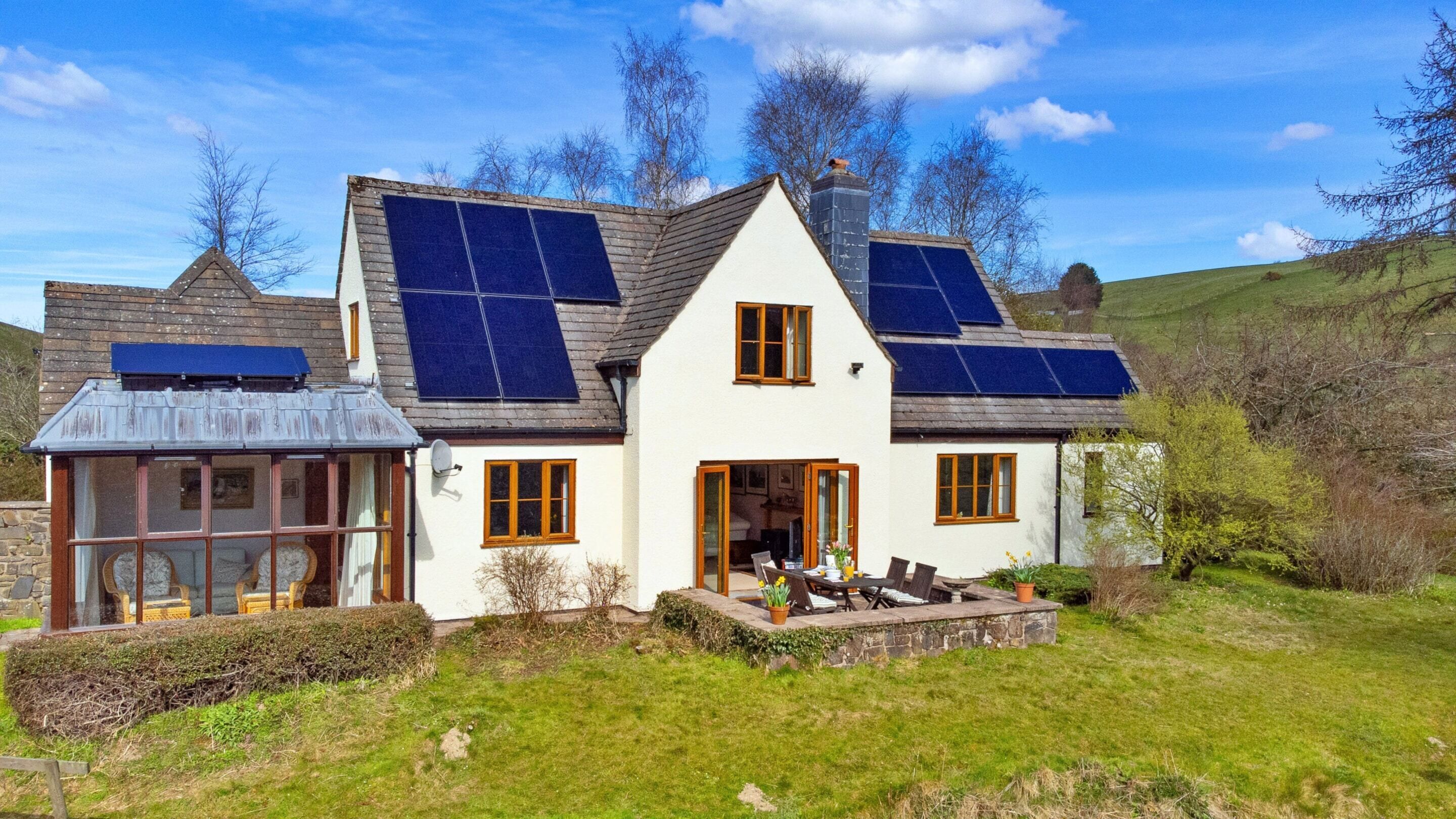 Een wit huis met zonnepanelen, een stenen oranjerie en een tuin.