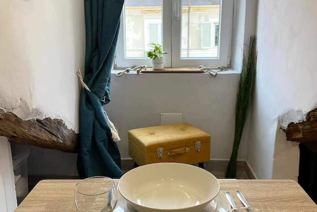 Ein Zimmer mit einem Holztisch, einer Schüssel, einem Glas, einem gelben Koffer und einem Fenster mit Vorhängen.