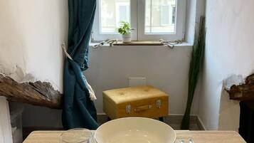 Ein Zimmer mit einem Holztisch, einer Schüssel, einem Glas, einem gelben Koffer und einem Fenster mit Vorhängen.