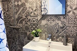 Un baño con baldosas estampadas, un lavamanos, una planta en maceta y una ducha.