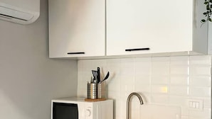 A kitchen with white cabinets, a microwave, a sink, and a utensil holder.