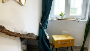 A room with a wooden table, a small yellow trunk, a window with curtains, and a plant on the windowsill.