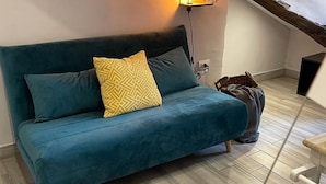 A teal sofa with patterned cushions in a room with wooden flooring and a visible electrical outlet.